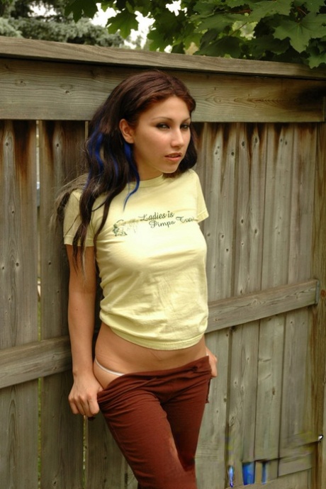 Brunette teen makes her nude modeling debut against a backyard fence